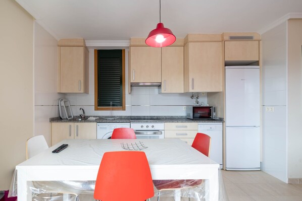 Una cocina compacta con armarios de madera, un refrigerador blanco, un microondas y una mesa de comedor con sillas rojas.