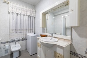 Un baño con inodoro, bidé, lavamanos, espejo y una cortina decorativa.