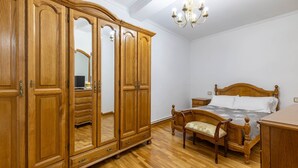 Un dormitorio con un armario de madera, una cama con cabecero de madera, una mesita de noche y una lámpara de araña.