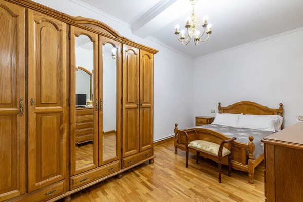 Un dormitorio con un armario de madera, una cama con cabecero de madera, una mesita de noche y una lámpara de araña.