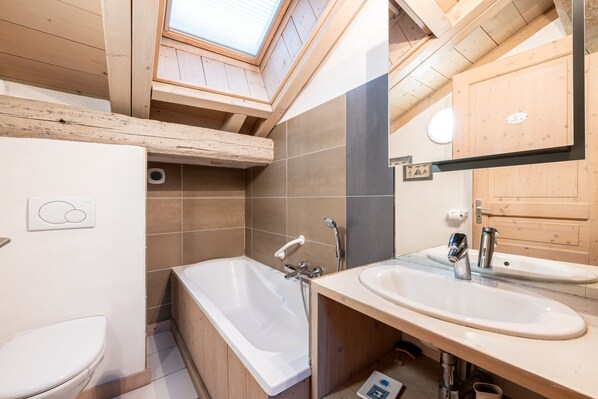 A modern bathroom with a skylight, a bathtub, a sink, and wooden cabinetry.