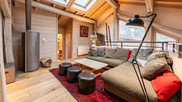 Un acogedor loft con chimenea, vigas de madera, un sofá, otomanas y un ventanal grande.