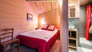Dormitorio de cabaña de madera con cama, una silla, una mesita de noche y un baño con lavamanos y ducha.