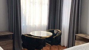 Ein Hotelzimmer mit rundem Tisch, zwei Stühlen, einem Bett, einem Nachttisch und einem Fenster mit Vorhängen.
