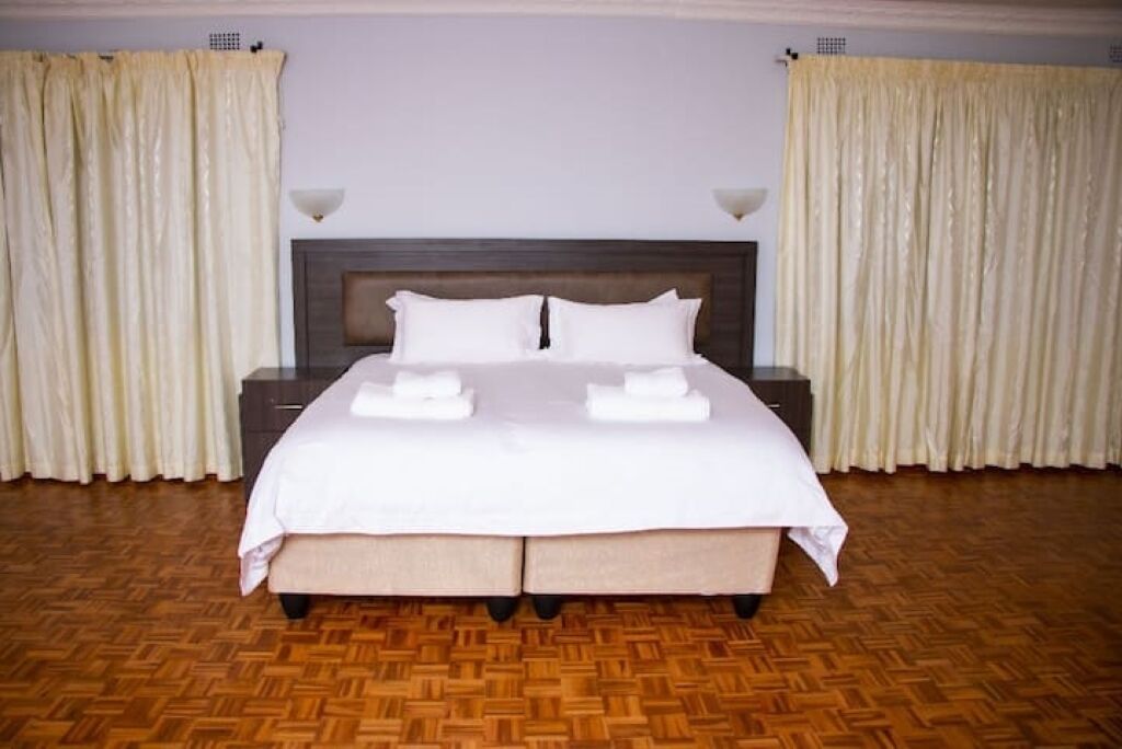 A neatly made bed with white linens, a wooden headboard, and a wooden parquet floor.