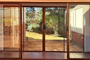 A sliding glass door leading to a backyard with a brick wall and greenery. - Mountain View Holiday Home

 (Harare)