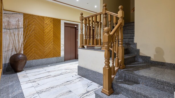 Un vestíbulo con suelo de mármol, una escalera de madera y una puerta, con un revestimiento de pared en patrón de espiga.