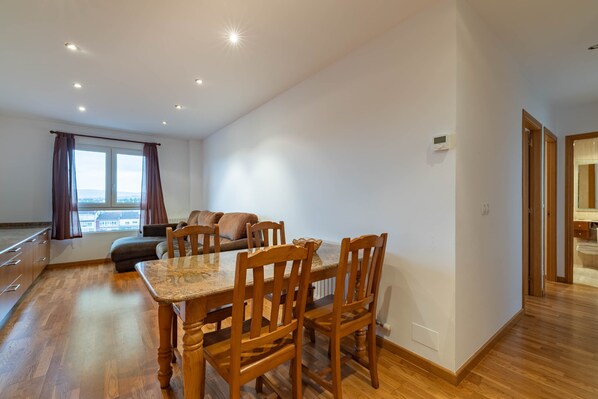 A modern living room with a dining area, wooden flooring, a large window with curtains, and a view of the city. - Celso Emilio Ferreiro Apartment in the Heart of Ribeira Sacra with Views of Monforte (Monforte de Lemos)