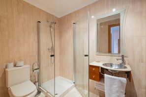 A bathroom with a glass-enclosed shower, a toilet, a sink, and a mirror. - Celso Emilio Ferreiro Apartment in the Heart of Ribeira Sacra with Views of Monforte (Monforte de Lemos)