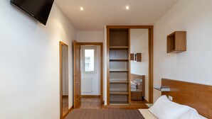 Un dormitorio con cama, cabecero de madera, televisor montado en la pared y armario empotrado con estantes.