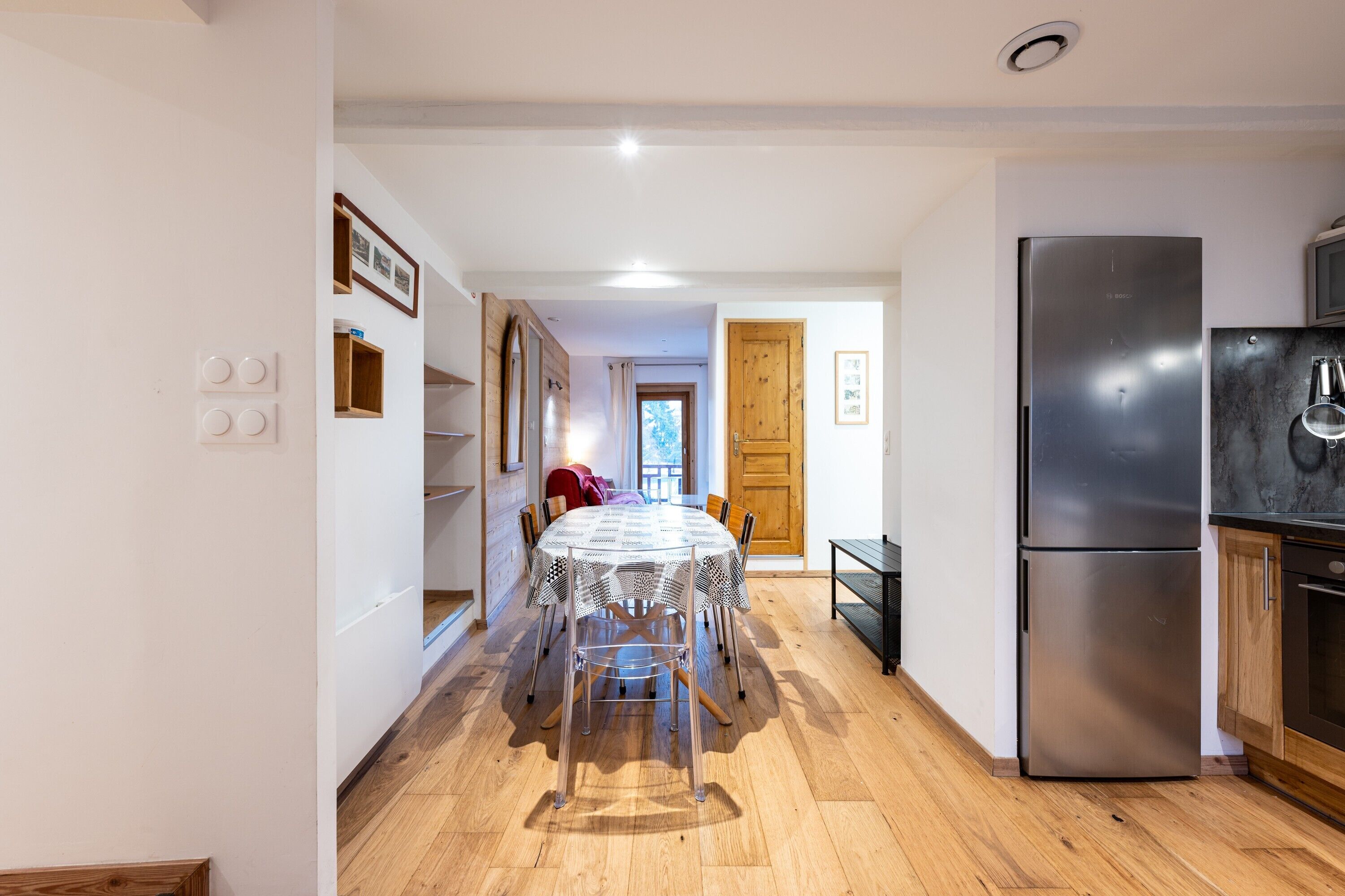 A kitchen with a dining table, chairs, a refrigerator, and wooden flooring.