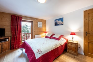 Een kamer met een bed, houten wanden, een televisie, een raam met gordijnen, een nachtkastje met een lamp en een deur.