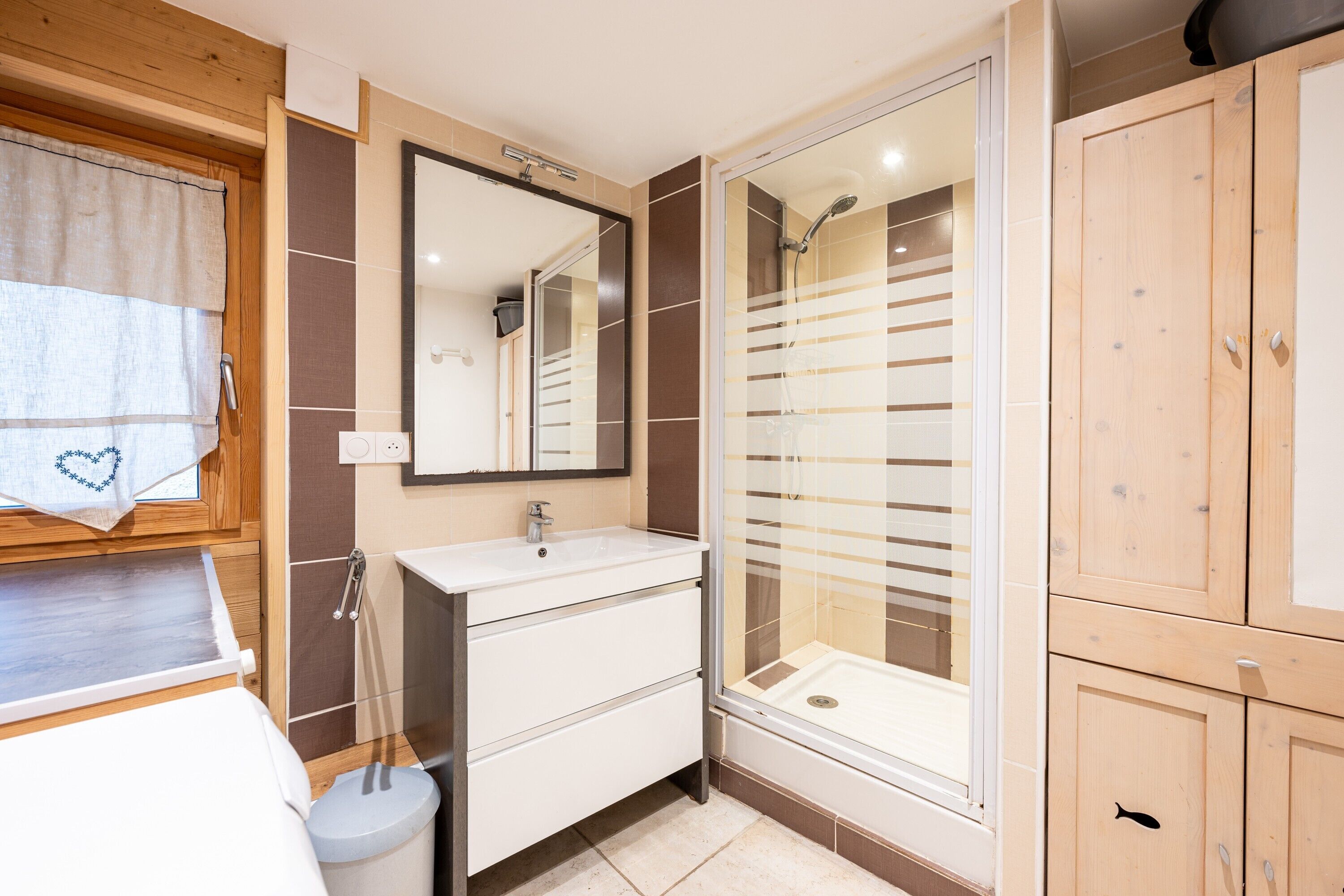 A bathroom with a sink, mirror, shower, and wooden cabinets.