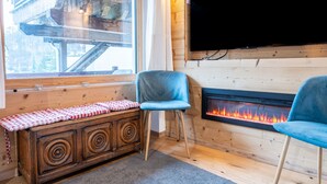 Une pièce chaleureuse avec un banc en bois, une chaise bleue, une cheminée et une grande fenêtre.
