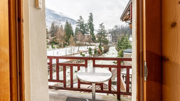 Un balcon en bois avec une table en métal, donnant sur un paysage enneigé parsemé d’arbres et de bâtiments.