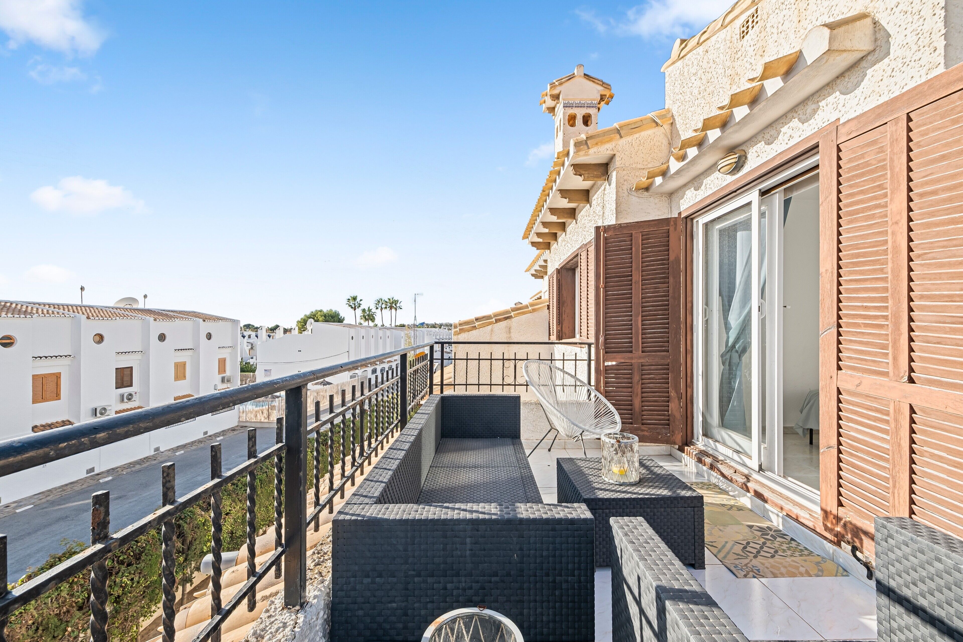 A balcony with a metal railing, a small seating area with a chair, and a view of the street and other buildings.