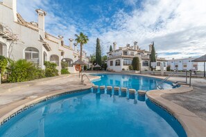 Una piscina con borde de azulejos, rodeada de edificios con ventanas arqueadas y cielo despejado.