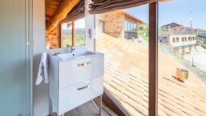 A modern bathroom with a large window, wooden ceiling beams, and a view of the surrounding buildings. - Casa Tunino with Shared Pool, Terrace, and Wi-Fi (Monforte de Lemos)