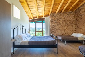 A bedroom with a bed, a small sofa, a window with curtains, and a stone wall.