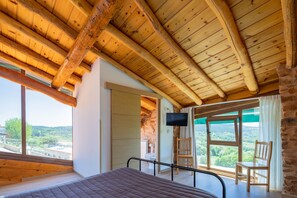 Un dormitorio con techo de madera, una cama, un televisor y vistas del paisaje.