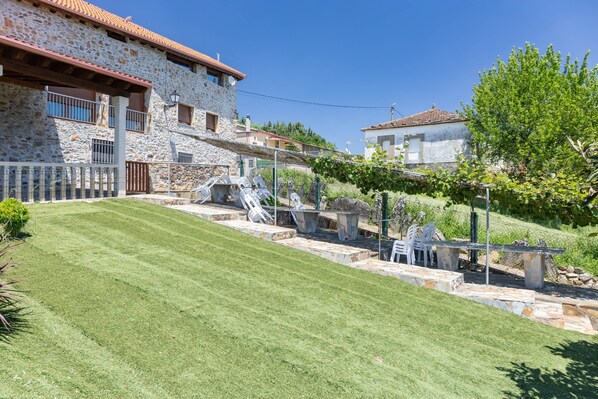 A stone building with a sloped roof, a paved patio with outdoor furniture, and a well-maintained lawn.