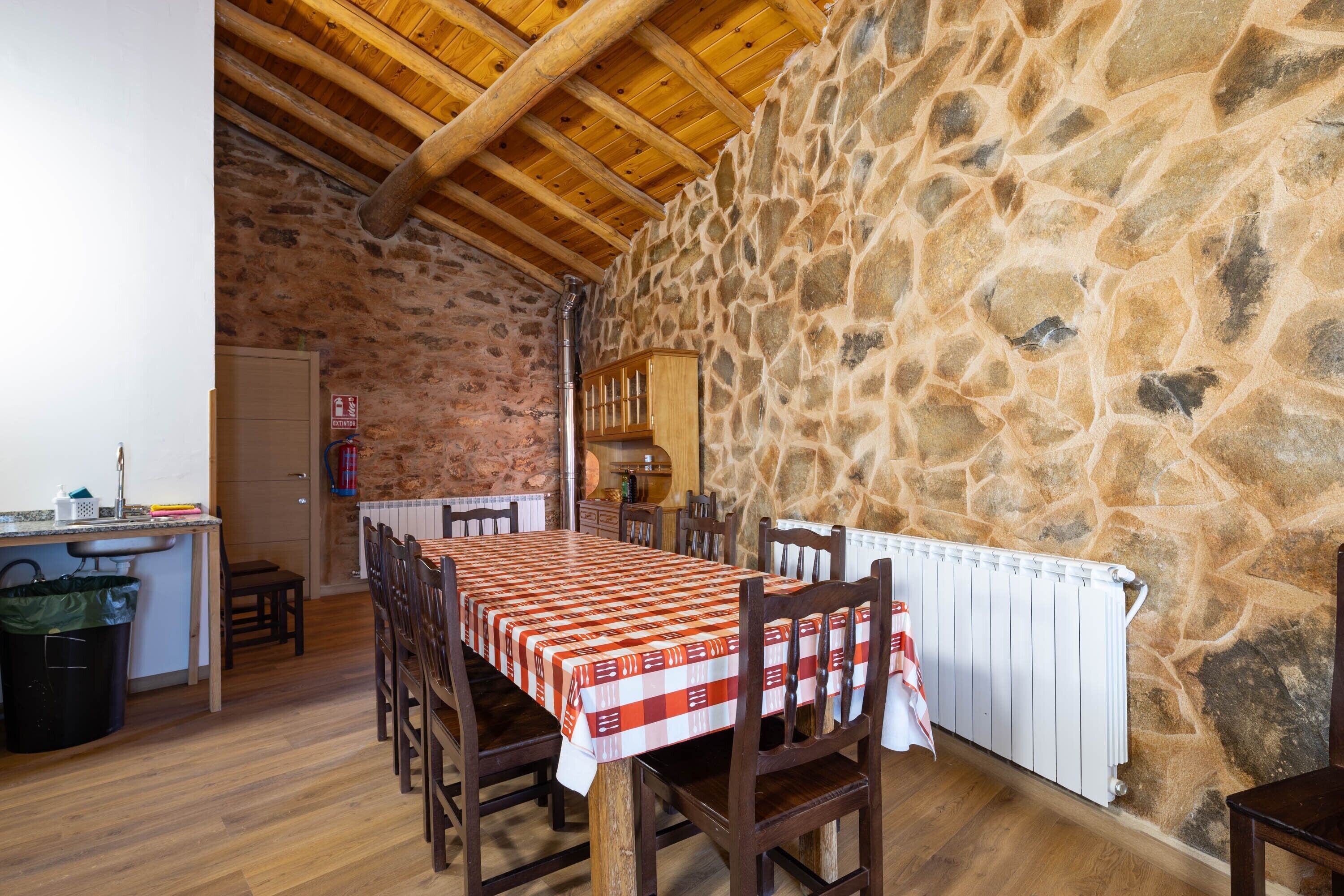 Un comedor con pared de piedra, techo de madera y una mesa lista para cuatro comensales.
