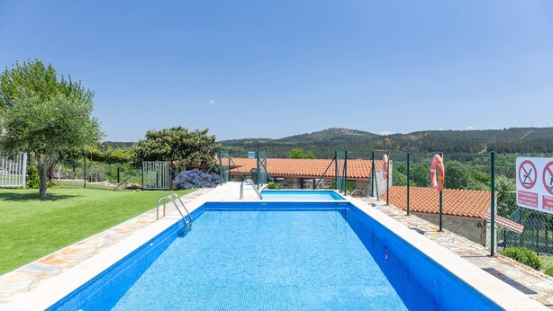 Une piscine rectangulaire à l’eau d’un bleu limpide, bordée de pierres et entourée d’une clôture en métal.
