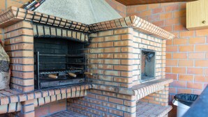 Un horno de ladrillo al aire libre con chimenea, un cubo de basura y un estante de madera.