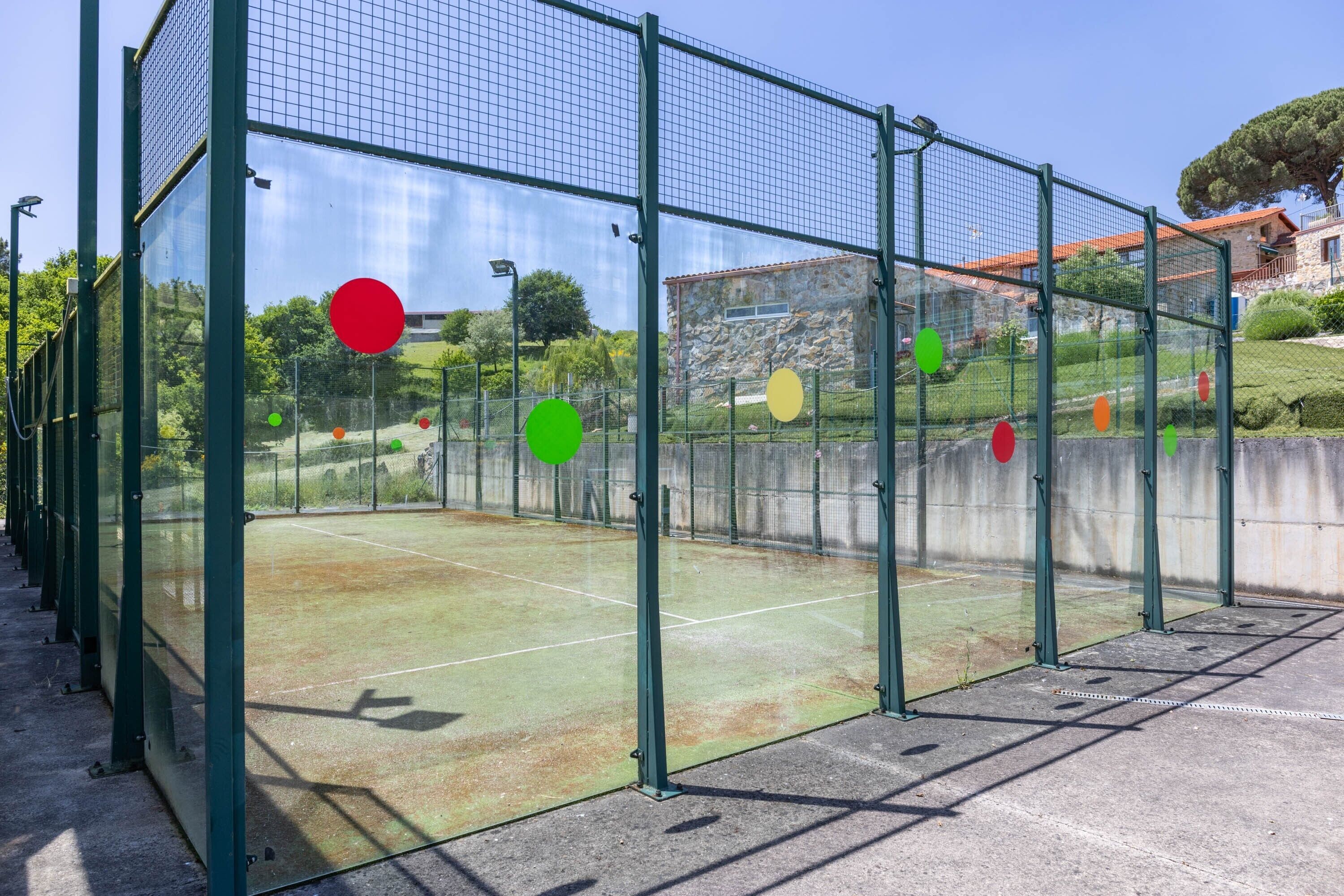 A tennis court enclosed by a green metal fence with a clear sky above.