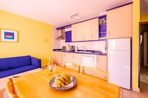 A compact kitchen with a dining table, a sofa, and a refrigerator.