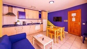 Una cocina compacta con electrodomésticos modernos, una zona de comedor con una mesa y sillas de madera, y un sofá.