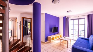 Una sala de estar con una escalera, un televisor de pantalla plana, un sofá azul y un banco de madera.