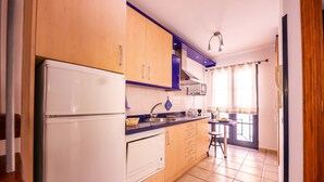Una cocina con armarios de madera, un refrigerador blanco, un fregadero y una ventana con cortinas.