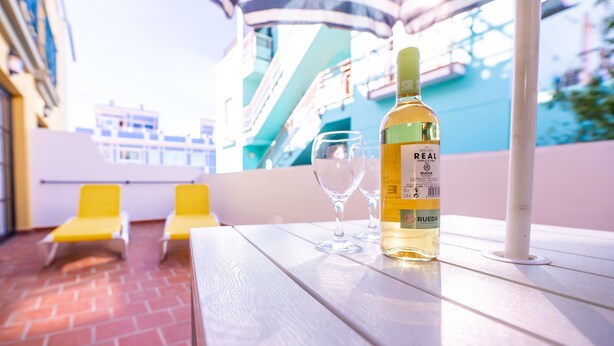 A table with a bottle of wine and glasses, yellow chairs, and a view of a building with balconies. - Apartment 'Nautilus 7' with Private Terrace and Wi-Fi (Puerto Naos)