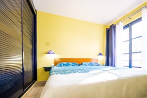 A hotel room with a bed, a nightstand, a lamp, and a window with curtains.