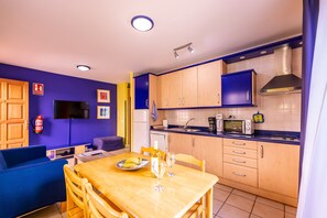 A compact kitchen with a dining area, a flat-screen TV, and a fire extinguisher.
