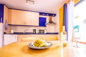 Une cuisine avec des meubles de rangement en bois, un four à micro-ondes, une machine à café, une assiette de bananes, une bouteille de vin et un verre à vin posés sur une table.