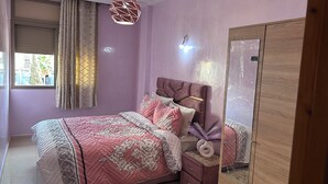 Un dormitorio con cama, mesita de noche, espejo y ventana con cortinas.