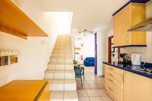Una cocina con armarios de madera, encimera azul y una escalera que lleva a otra habitación.