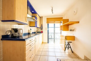 Una cocina con armarios de madera, cafetera y ventana con persianas.