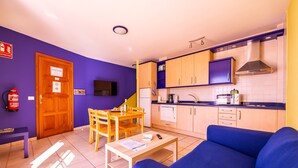 A compact living space with a kitchenette, a sofa, a dining table with chairs, and a television.