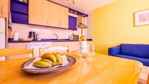 A kitchen with a dining table, chairs, a plate of bananas, a bottle of wine, and glasses.