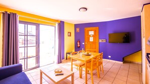 A room with a dining table, chairs, a sofa, a television, and a sliding glass door.