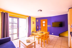 Ein Zimmer mit Esstisch, Stühlen, einer Couch, einem Fernseher und einer Schiebetür.