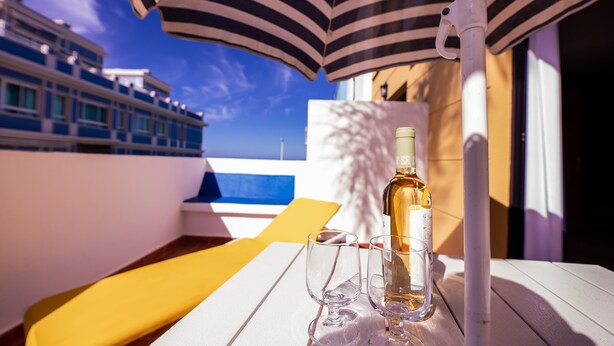 A table with a bottle and glasses, a striped umbrella, and a view of a cruise ship.