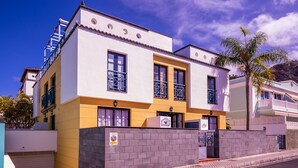 Un edificio de dos pisos con fachada blanca y amarilla, una entrada con reja y cielo despejado.