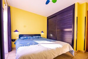 Ein Zimmer mit einem Bett, zwei Nachttischlampen, einem Deckenventilator und einem Fenster mit Vorhängen.