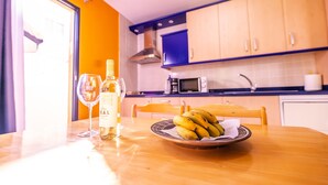 Una cocina con armarios de madera, un microondas y una mesa de comedor con un plato de plátanos y una botella de vino.