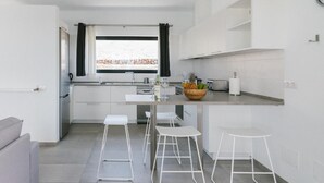 Una cuina moderna amb armaris blancs, una illa central amb tamborets, una finestra amb cortines i vista a un paisatge rocos.
