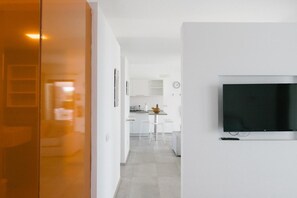 Ett modernt kök med vita skåp, en matplats med barstolar och en platt-TV som är monterad på väggen.